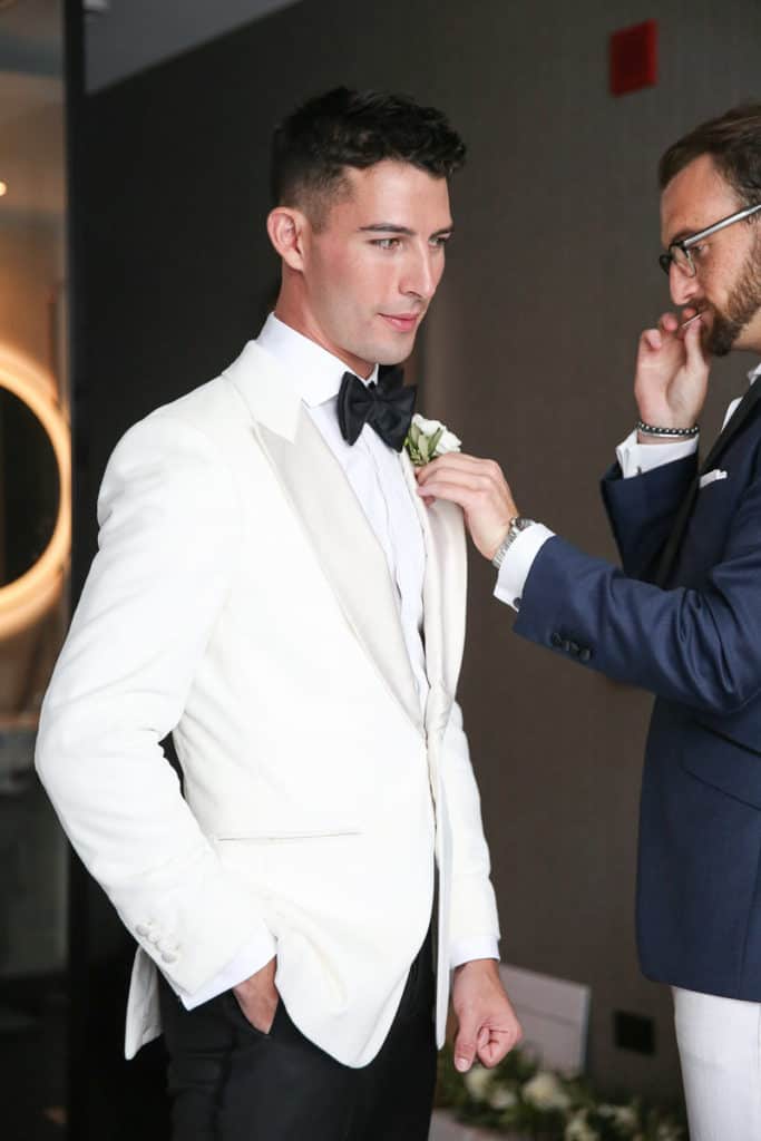 G ALXNDR owner Grant Alexander pinning the boutonniere of one of his grooms on wedding day. Part of what the best wedding dresser and wedding stylist services are.