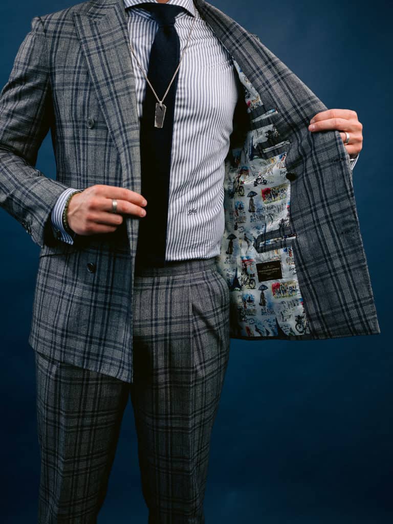 Custom suit in grey and navy plaid fabric with a fun lining on the inside, a navy tie, and jewelry.