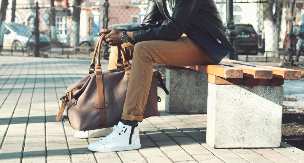 G ALXNDR client in cool casual street style with weekender bag, white sneakers, brown denim, and a jacket